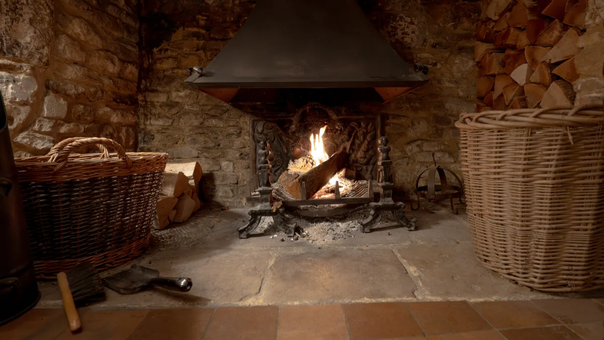 A log fire burning in the stone inglenook fireplace at Well Cottage, with baskets of logs either side