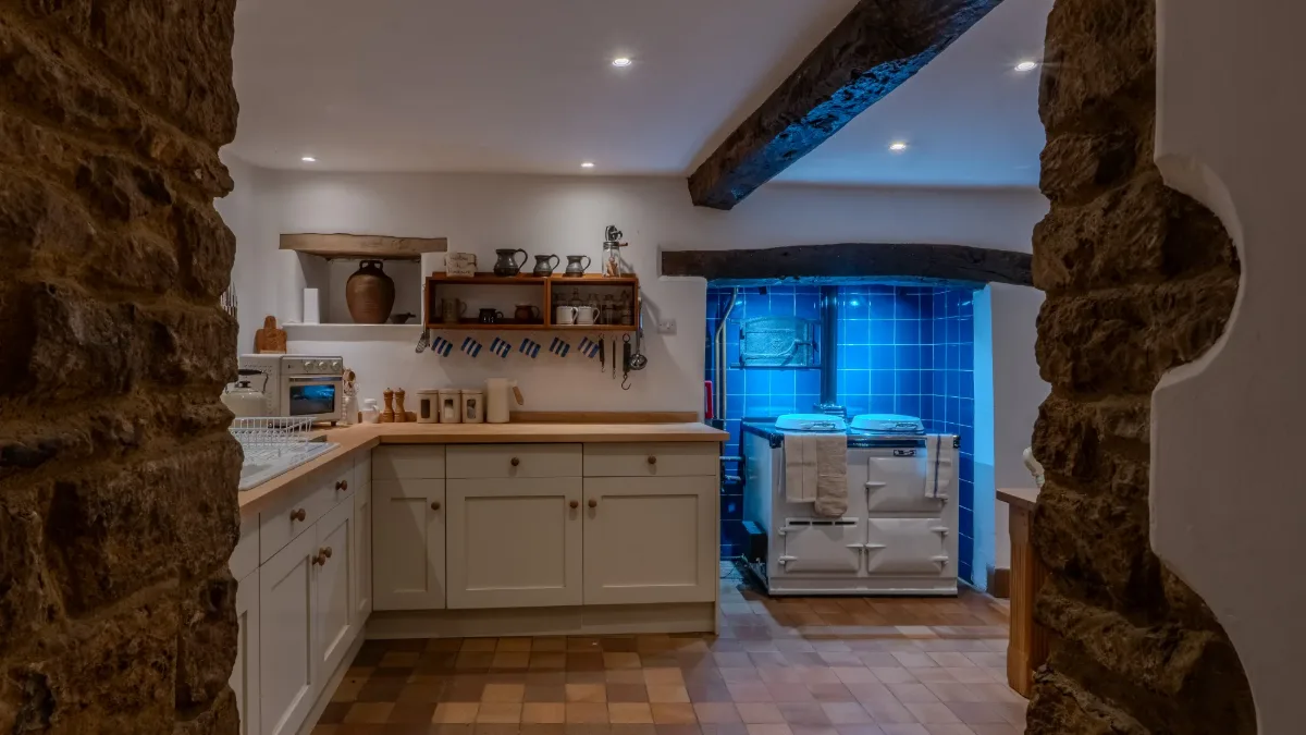 The farmhouse kitchen at Well Cottage with a cream Aga, seen through a stone archway
