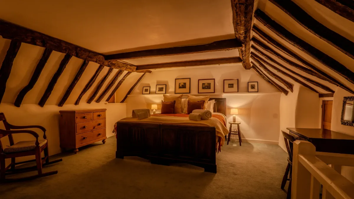 The super-king bedroom at Well Cottage under the eaves, warmly lit beneath old oak beams