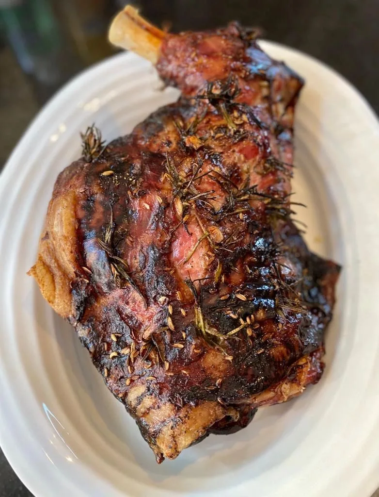 Sophie's slow-roast lamb, glazed dark and studded with rosemary and fennel seeds, on a white platter