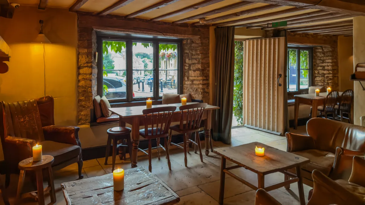 The candlelit, low-lit interior of The Bull, Charlbury, with stone walls, beams and leather chairs