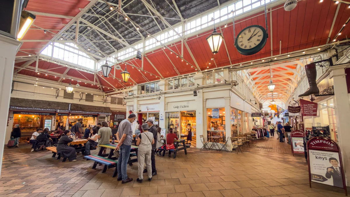 The old market clock above the avenues of Oxford Covered Market, with cafés, a bookshop and the cobbler's sign nearby