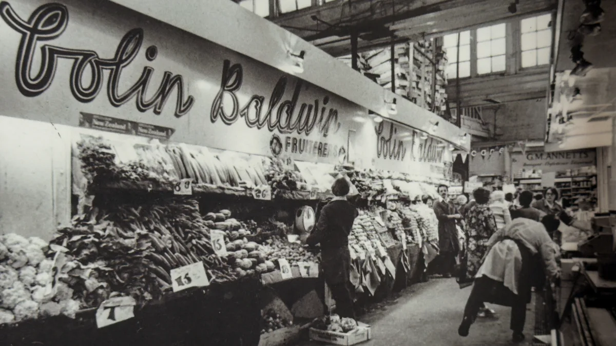 Colin Baldwin's fruit and vegetable stall in Oxford Covered Market, laid out in long rows with shoppers browsing