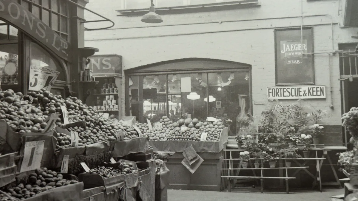 A greengrocer's stall in Oxford Covered Market in the early twentieth century, produce stacked high beneath painted shop signs