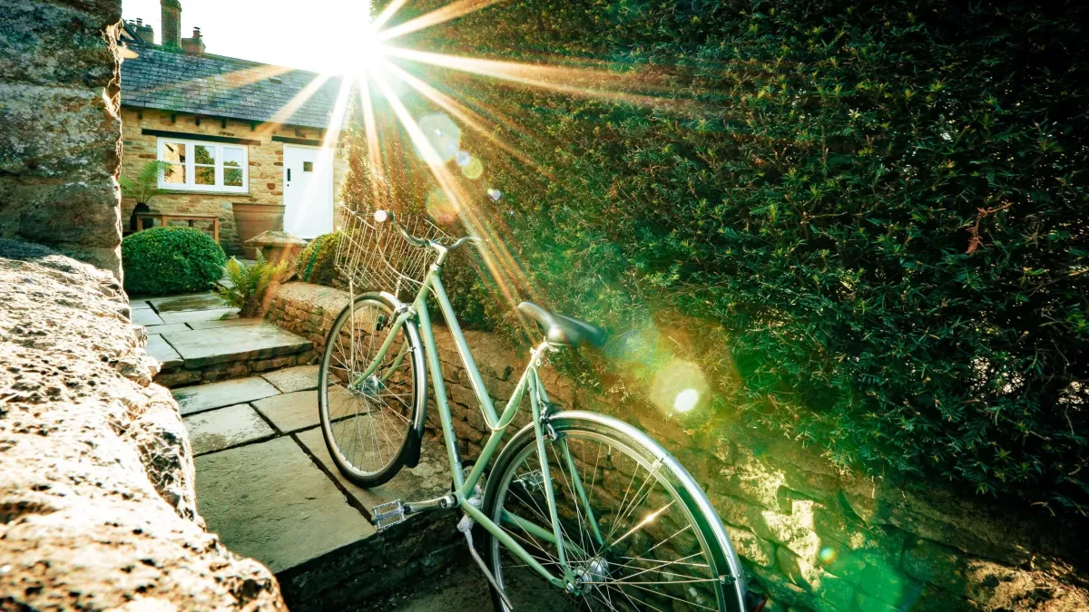 A green Soho Farmhouse bicycle leaning against a wall outside Well Cottage in the sunshine