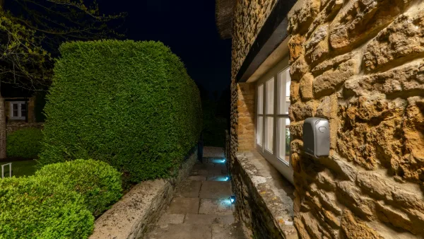 The side path at night with blue LED ground lights along the stone wall and clipped hedge