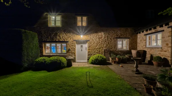 The cottage at night, stone walls lit by the porch lantern and box hedging dark in the foreground