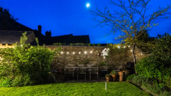 The walled garden at night under a full moon, festoon lights strung over the dining table
