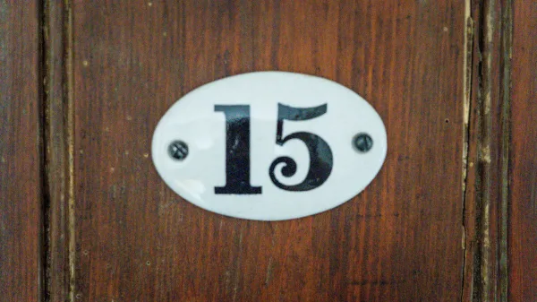 Enamel number plate reading 15 on a dark oak door