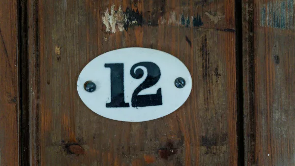 Enamel number plate reading 12 on a weathered oak bedroom door