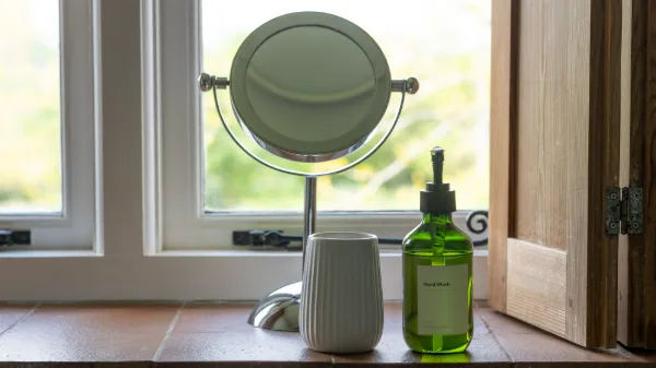 A vanity mirror, toothbrush holder and hand wash on the stone windowsill