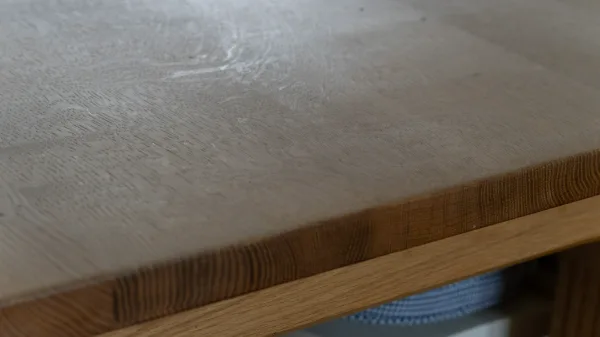 Close-up of the worn oak worktop edge, grain and flour dust caught in the light