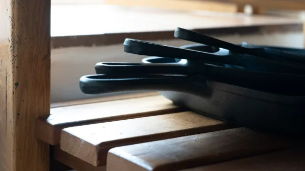 Cast-iron skillets stacked on an oak shelf, side-lit in warm shadow