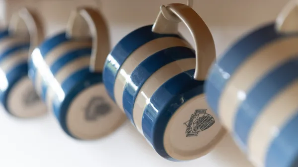 Blue-and-white striped Cornishware mugs hanging from hooks beneath the shelf