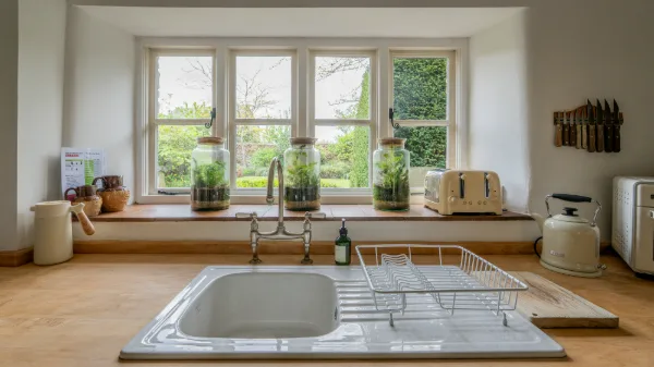 The kitchen sink beneath a bay window with glass terrariums and a view of the garden