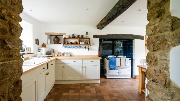 Cream cabinets and oak worktop seen through stone pillars, the Aga in its blue-tiled alcove