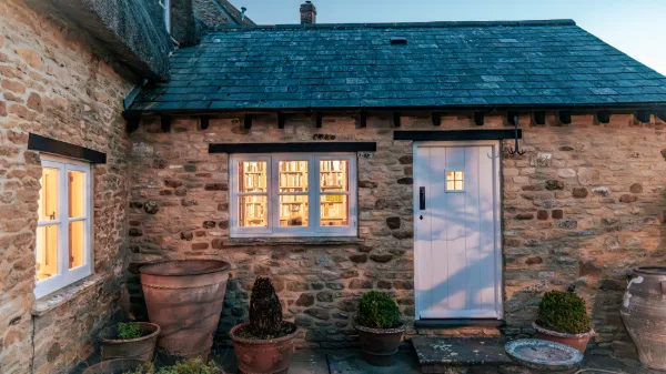 The stone outbuilding at dusk, warm light in the windows and terracotta pots by the door