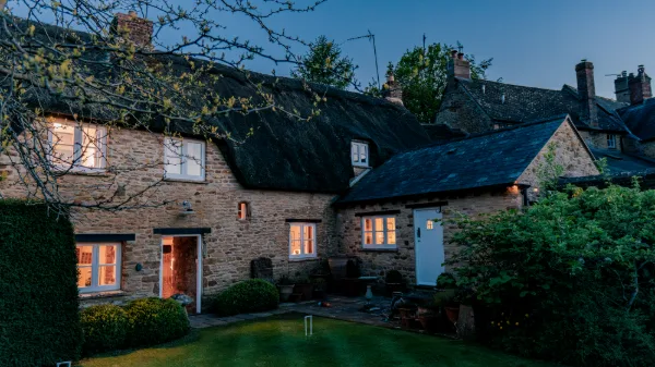 The full cottage frontage at blue hour, croquet hoops on the lawn and warm light in every window