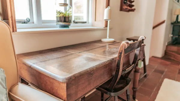 An old writing desk by the window with a candle lamp, quarry-tile floor