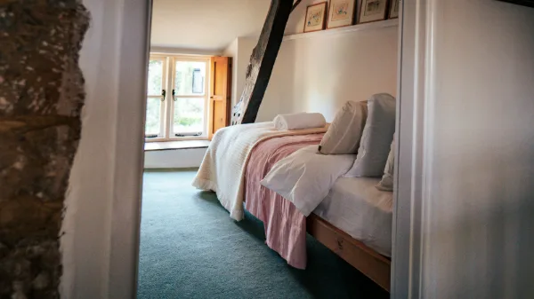 The single bedroom through the doorway: pink bedding, curved beam overhead and a shuttered window