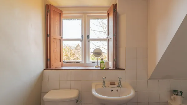 The ensuite basin and toilet beneath a shuttered window with a round vanity mirror