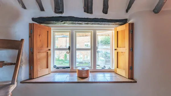A bedroom window with pine shutters open, dark beams above and a view of the hamlet