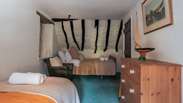 The twin bedroom with exposed cruck beams, leather armchair and a pine chest of drawers
