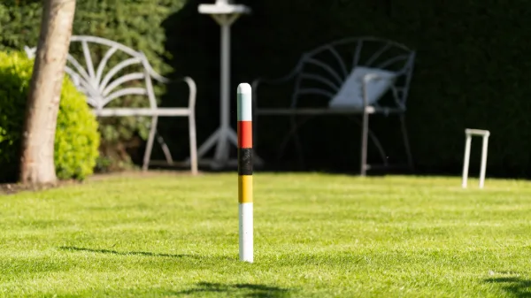 A croquet peg on the walled lawn, metal garden chairs in the shade beyond