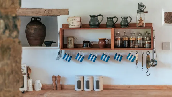 Open kitchen shelves with striped mugs, pewter jugs, spice jars and an old olive jar