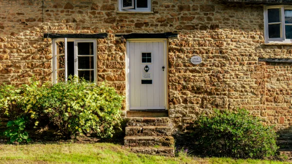The front door of Well Cottage, white stable door and stone steps up to honey-coloured walls
