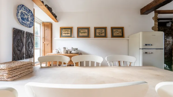 The dining end of the kitchen with fish prints on the wall, white chairs and a cream fridge