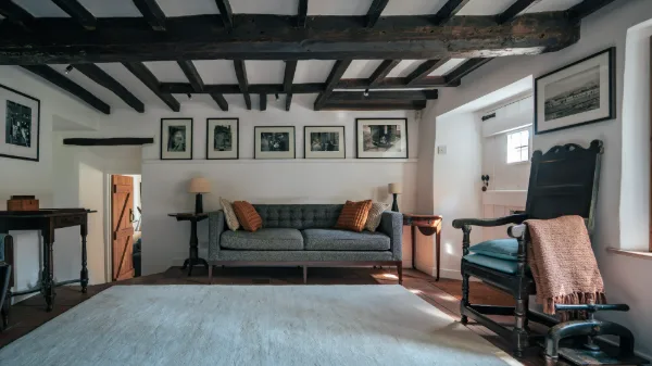The sitting room: dark oak beams overhead, grey sofa, framed prints and an antique rocking chair