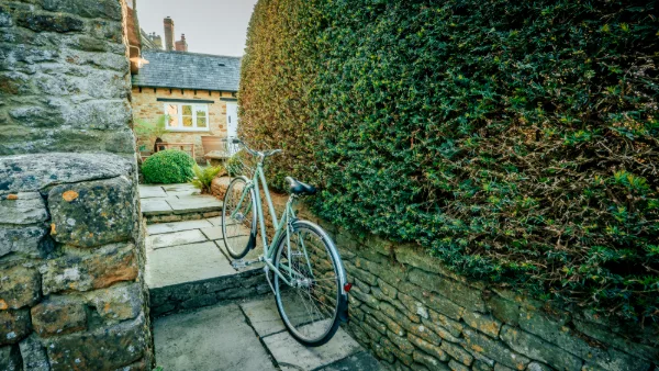 A vintage bicycle leaning against the stone wall by the garden gate, clipped hedge behind