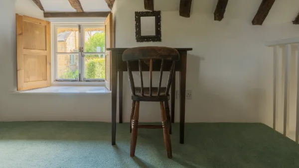 A wooden desk and farmhouse chair by the open shuttered window under dark beams