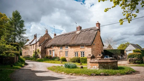 The front of Well Cottage in morning sun: honey-stone walls, thatched eaves and the cottage well in the foreground