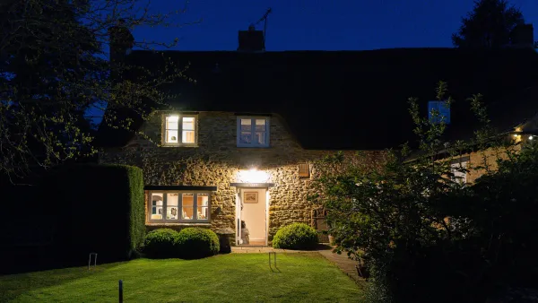 Well Cottage at dusk, its windows glowing warm amber against the deep blue evening sky and clipped garden hedges