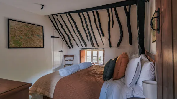 The king bedroom with dramatic dark oak beams across a sloping ceiling, a framed local map and crisp white linen