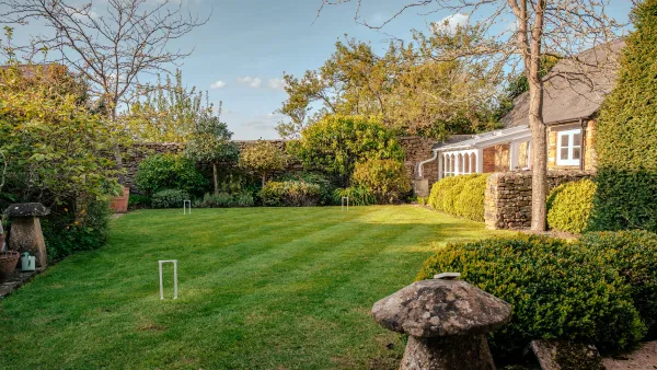 The walled garden with a croquet lawn, mature shrubs and a glimpse of the cottage garden room in afternoon light