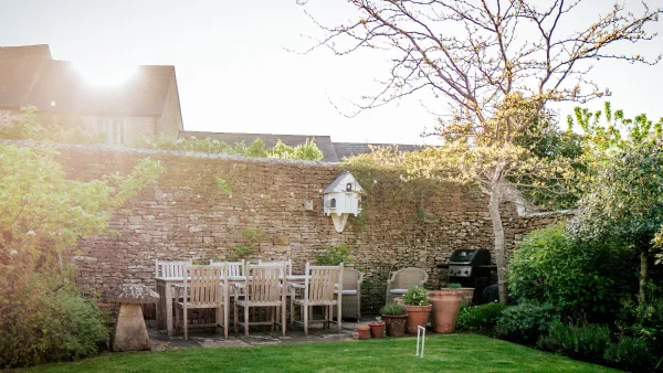 The garden dining area against a dry-stone wall in low evening sun, with the gas barbecue and potted plants nearby