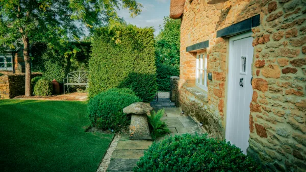 The garden door and staddle stone beside clipped box hedging, the lawn stretching to the greenhouse