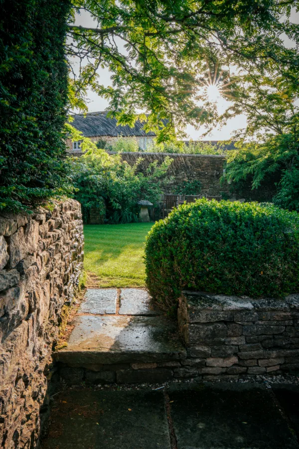 Sunlight bursting through the trees at the garden gate, stone walls and clipped box beyond