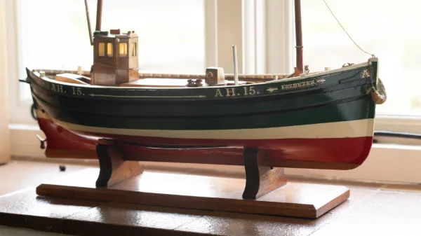 A model fishing boat named Ebenezer on the bathroom windowsill, green hull and red keel