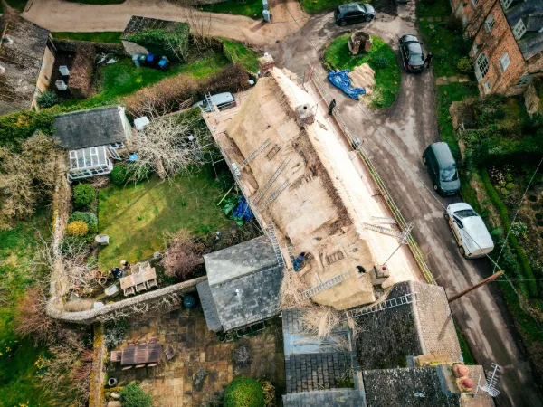 Aerial view directly above the cottage: the long roof stripped bare, garden and lane on either side