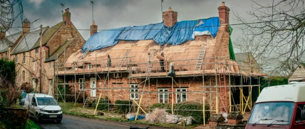 The cottage mid-rethatch, scaffolding up and the old thatch stripped back to bare rafters