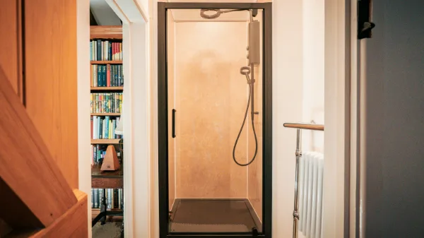 The shower room with glass door and rainfall head, a bookshelf glimpsed through the doorway