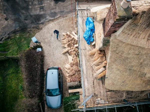 Straw bales stacked beside the cottage ready for the rethatch, a thatcher crossing the driveway below