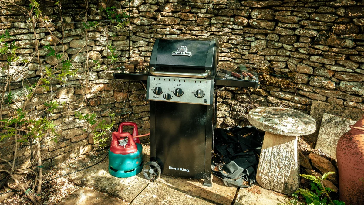 The black gas BBQ at Well Cottage standing against the honey-coloured dry-stone wall, its gas bottle alongside and a staddle stone to one side