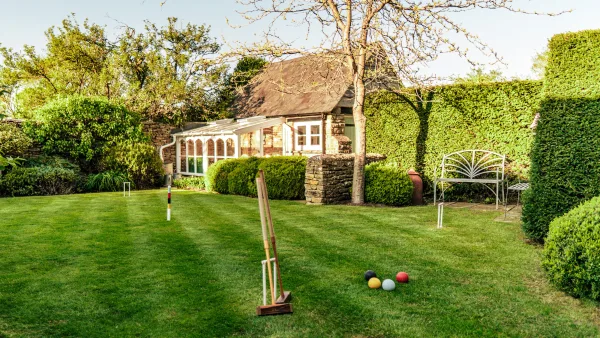 A game of croquet underway on the sunlit lawn of Well Cottage, mallets and hoops set out on the short grass