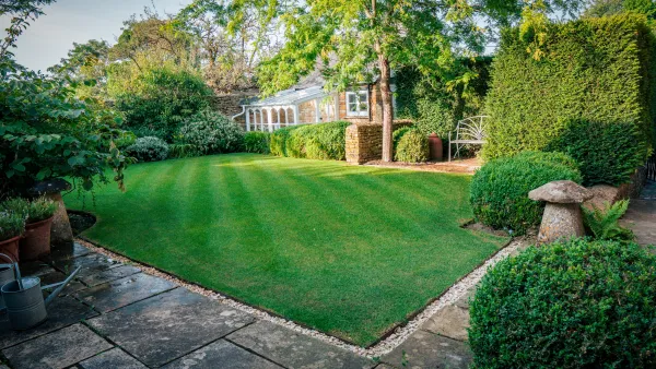 The walled garden at Well Cottage in golden evening light, the full sweep of striped lawn running up to the conservatory
