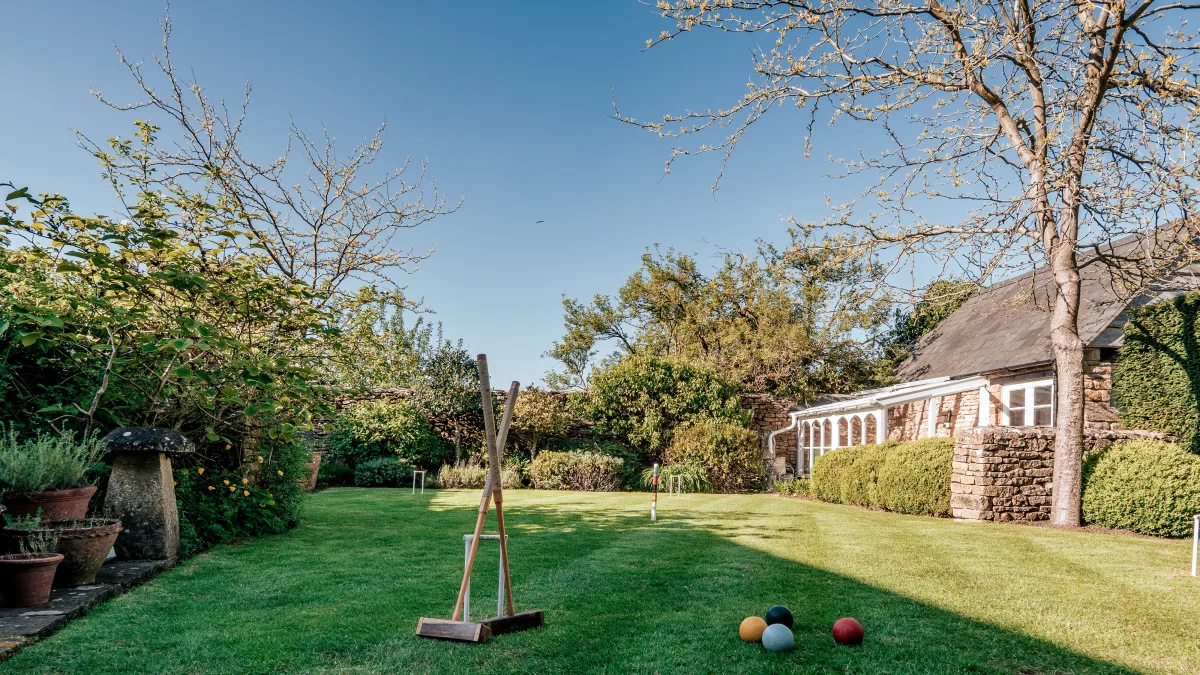 The lawn at Well Cottage under a deep blue sky, a croquet mallet leaning on its stand with the conservatory and clipped hedges in the distance
